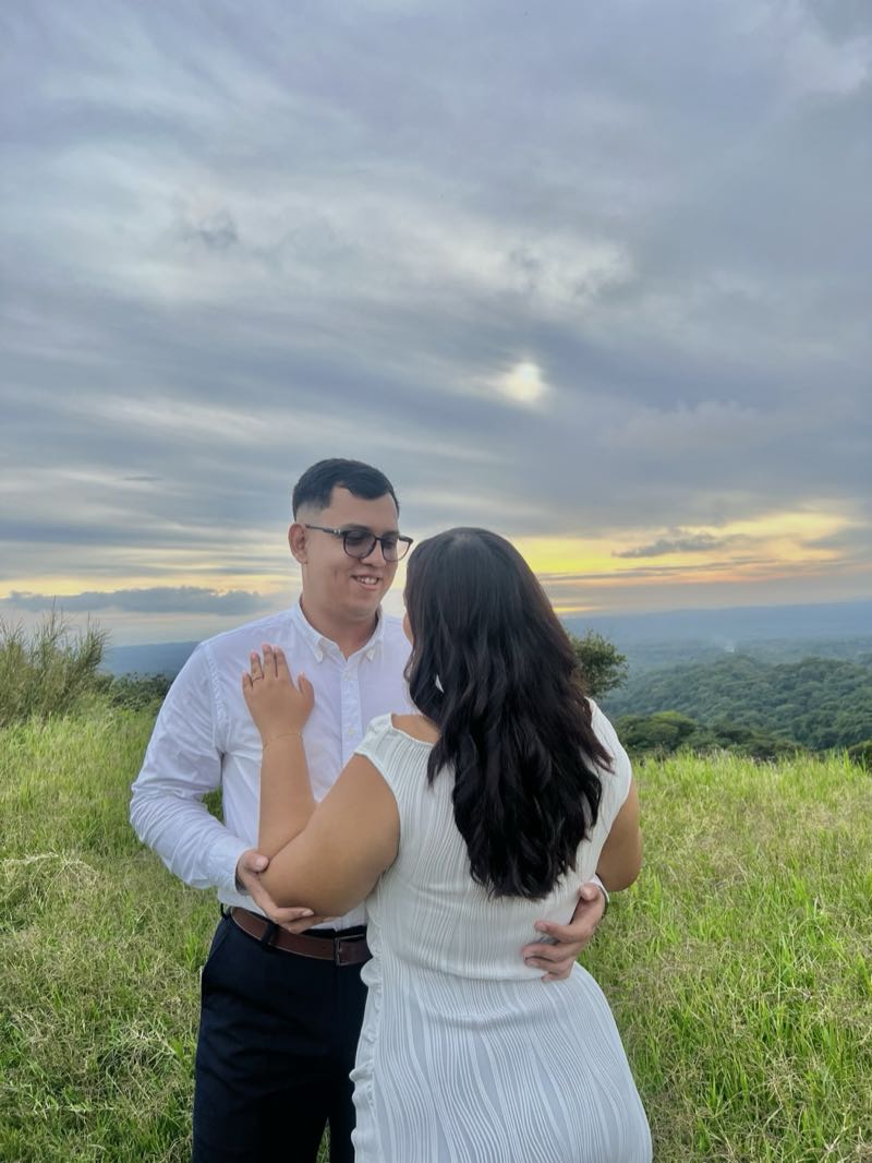 Byron y Jennyfer abrazados frente al valle, él sonriéndole